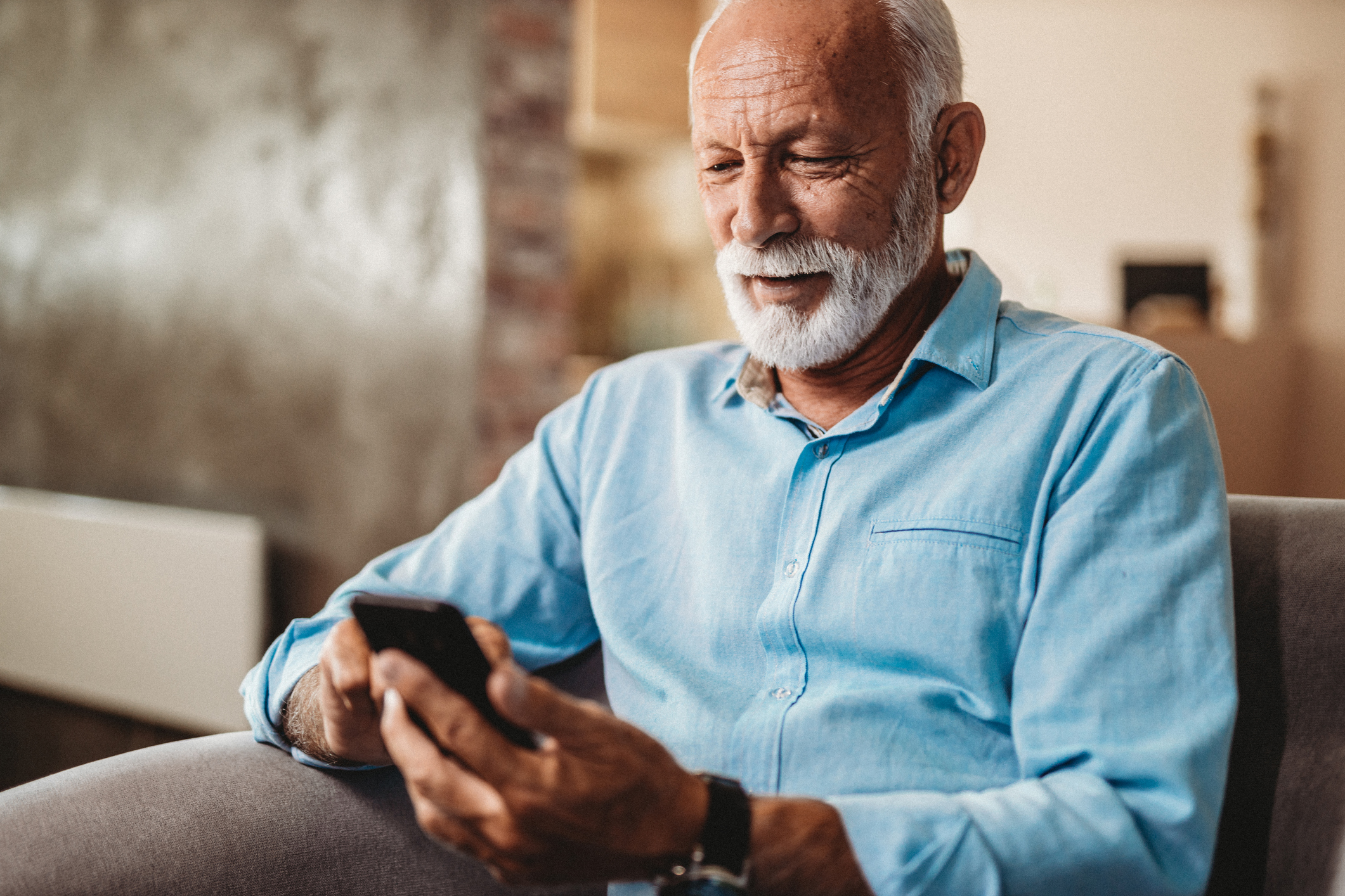 Older Christian man smiling happily while using mobile phone